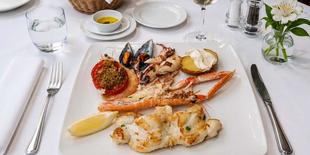 Assiette de poissons et fruits de mer servie au restaurant espagnol El Faro à Genève, accompagnée de légumes et de vin blanc espagnol.