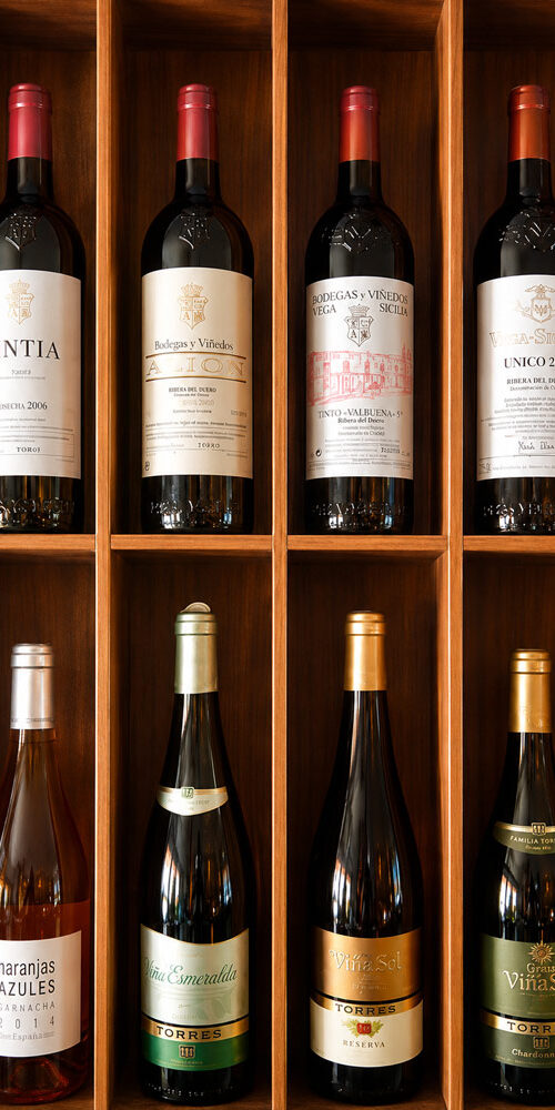 Présentation de bouteilles de vin rouge et blanc espagnol soigneusement rangées dans un casier en bois de la cave du restaurant El Faro situé aux Pâquis à Genève