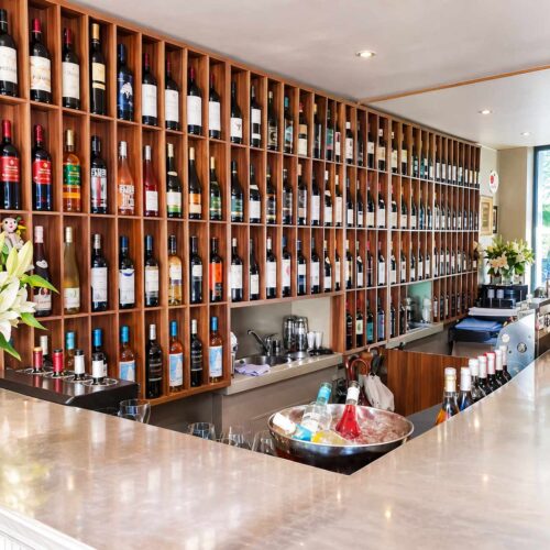 Vue d'ensemble d'un grand mur de casiers en bois remplis de bouteilles de vin derrière le comptoir du bar du restaurant El Faro situé dans le quartier des Pâquis à Genève