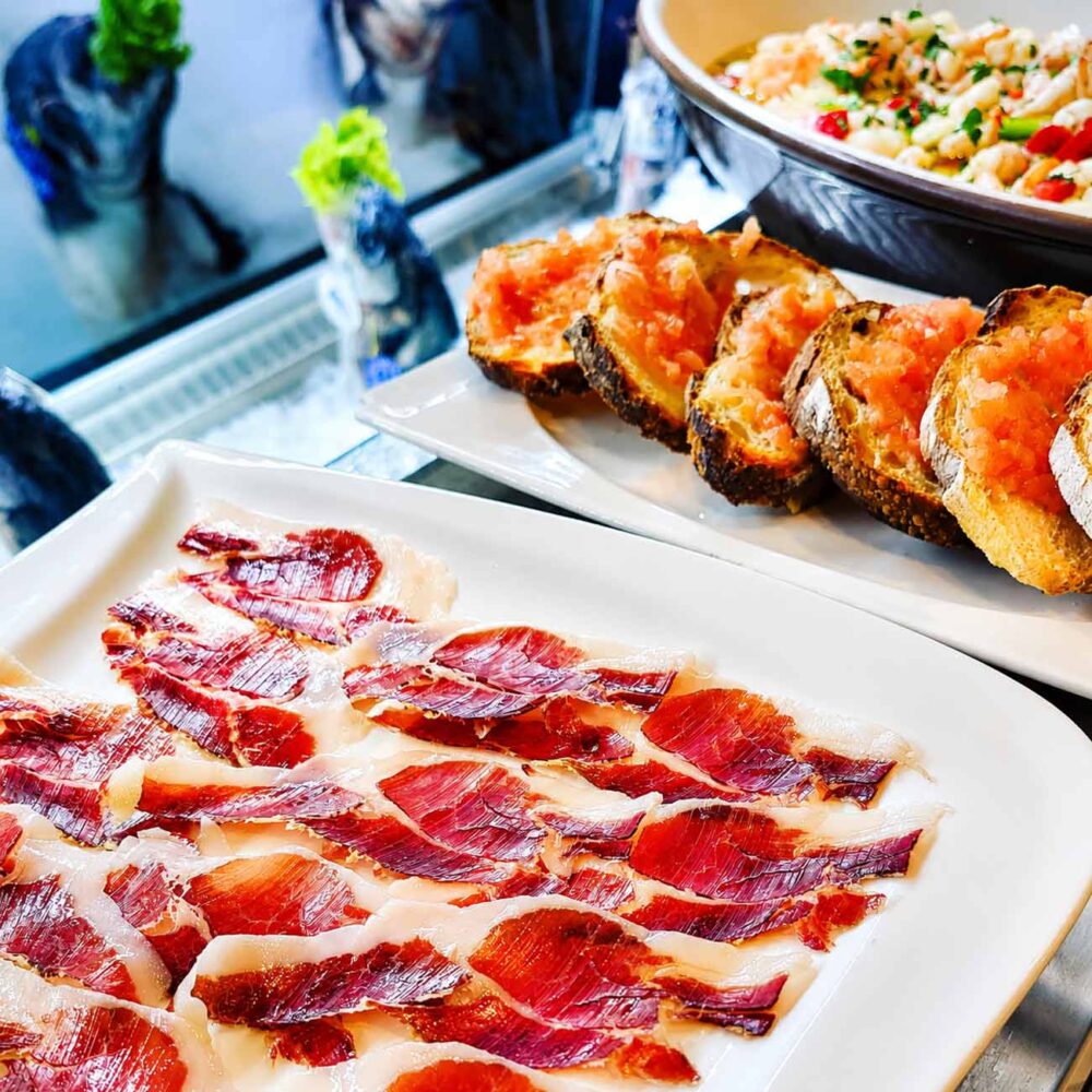 Assiette de fines tranches de jambon ibérique accompagnées de pain à la tomate et de tapas, servies au restaurant El Faro dans le quartier des Pâquis à Genève