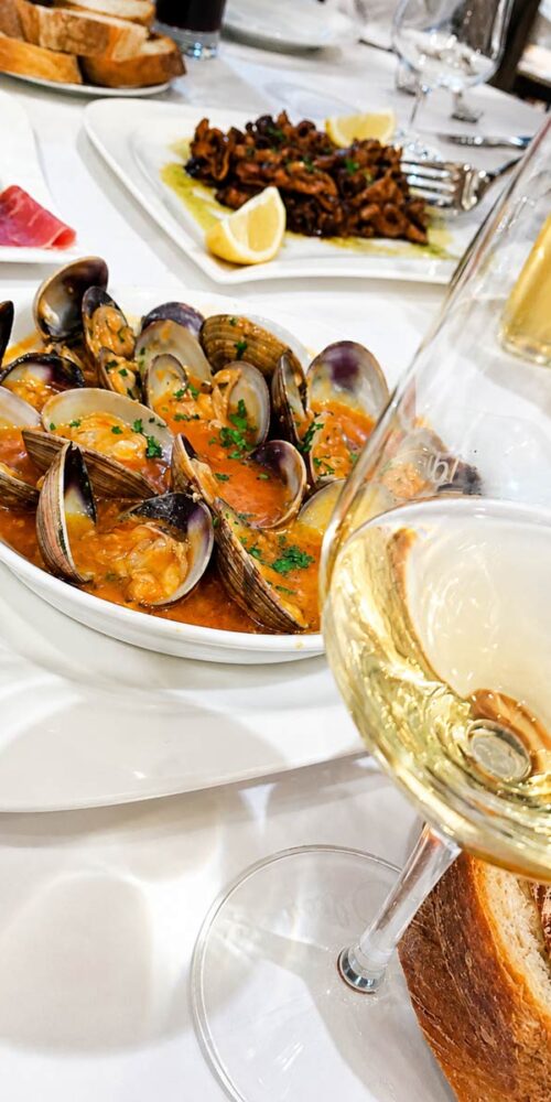 Assiette de palourdes en sauce accompagnées d'un verre de vin blanc au premier plan, servies au restaurant El Faro dans le quartier des Pâquis à Genève