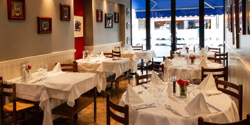 Vue de la salle de restaurant élégamment dressée du restaurant El Faro, avec ses tables nappées et ses chaises en bois, située aux Pâquis à Genève