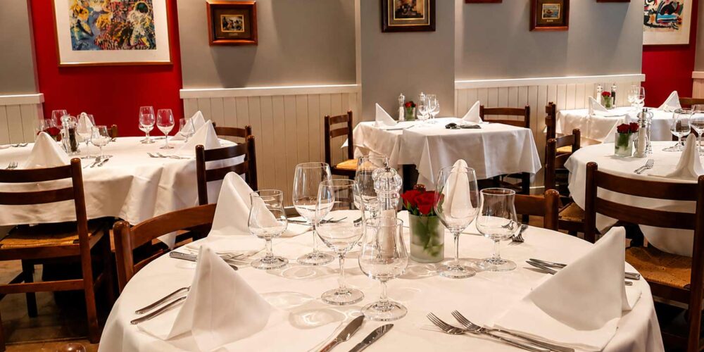 Gros plan sur des tables élégamment dressées avec des nappes blanches, des couverts en argent et des verres à pied prêts pour le service au restaurant El Faro aux Pâquis à Genève