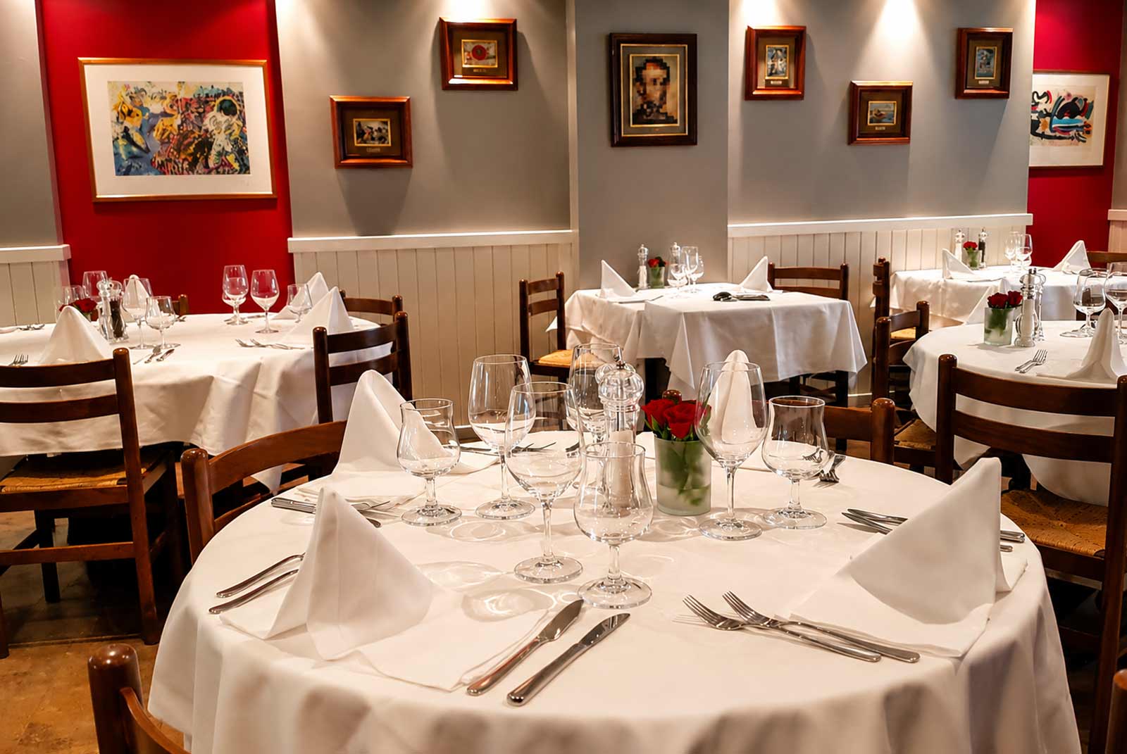 Gros plan sur des tables élégamment dressées avec des nappes blanches, des couverts en argent et des verres à pied prêts pour le service au restaurant El Faro aux Pâquis à Genève